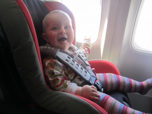 Zufriedenes Baby im Autokindersitz im Flugzeug